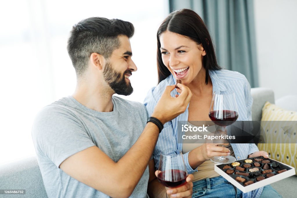woman couple man happy happiness  love young chocolate praline eating together romantic boyfriend girlfriend Portrait of a lovely young couple eating chocolate praline together on sofa  at home Chocolate Stock Photo