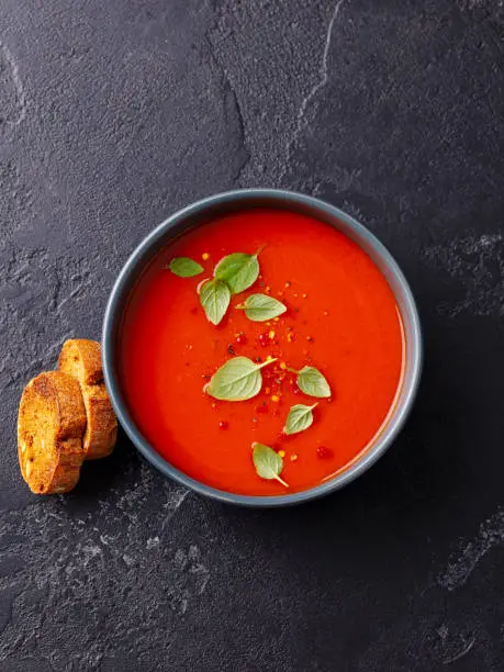 Tomato soup with basil in a bowl. Dark background. Top view.