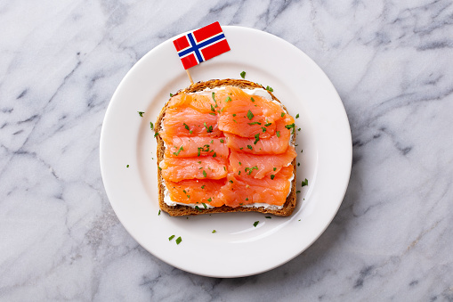 Sandwich, toast with smoked salmon and cream cheese on white plate. With Norwegian flag. Marble background. Top view.
