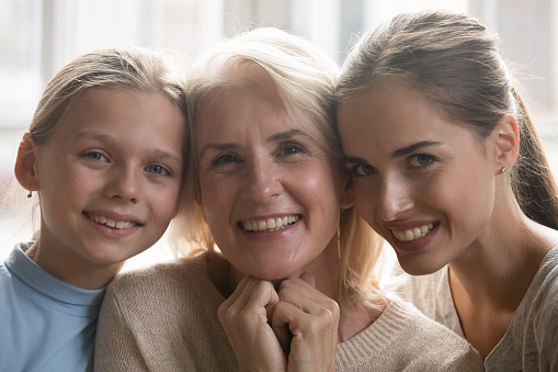 Family portrait of beautiful happy three generations of women hug look at camera smiling, excited senior 60 woman posing with millennial daughter and preschooler granddaughter, heritage concept