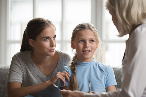 Young mother and little daughter visit female doctor talk about health complains, woman pediatrician consult girl with mom, make notes in card, write medicine prescription, children healthcare concept