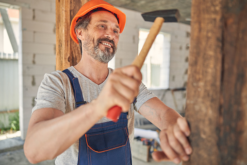 Front view of an attractive man in a helmet driving a nail with a hammer