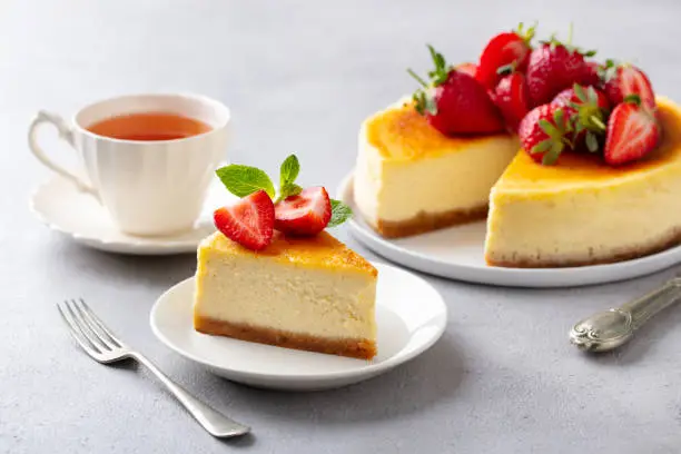 Cheesecake dessert with fresh strawberries and cup of tea. Grey background.