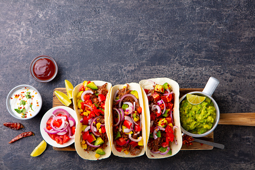 Taco with meat and vegetables on cutting board. Grey background. Copy space. Top view.