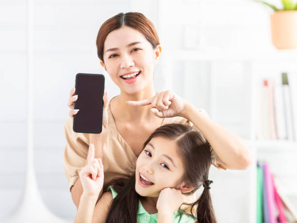 mère et fille heureuse montrant le téléphone portable - mother holding child pointing photos et images de collection