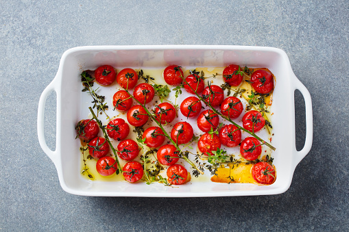 Roasted cherry tomatoes in baking dish. Grey background. Close up. Top view.