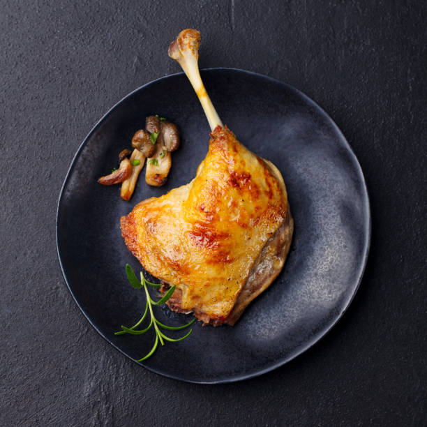 Duck leg confit with mushroom sauce on black plate. Slate background. Top view. Duck leg confit with mushroom sauce on black plate. Slate background. Top view. confit stock pictures, royalty-free photos & images