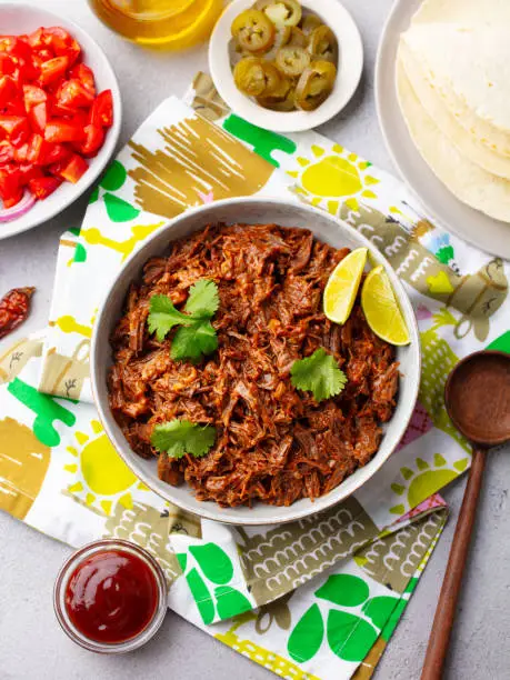 Mexican shredded beef with tortillas, vegetables and sauce. Grey background. Top view.