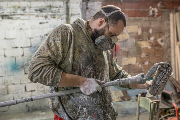 istock A man with a mask is holding a long paint roller in a messy room 1265531149