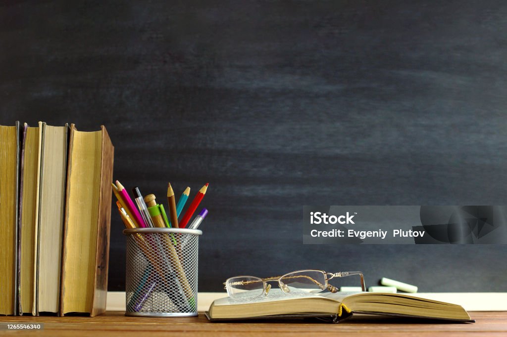 Glasses teacher books and a stand with pencils on the table, on the background of a blackboard with chalk. The concept of the teacher's day. Copy space. Teachers' Day Stock Photo