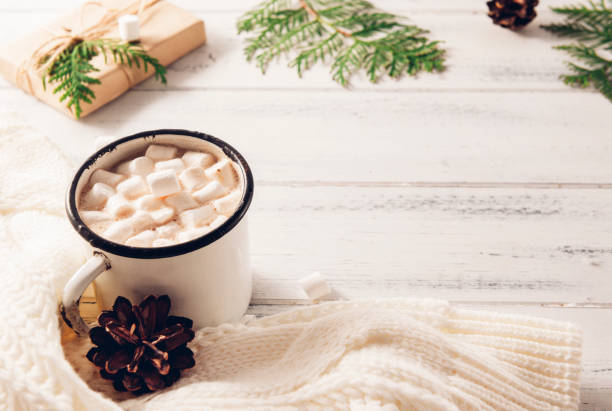 istock cocoa mug with marshmallows, white sweater, cones, gift box, green branches of thuja, fir branches on a white wooden background, hot winter drink 1265548367