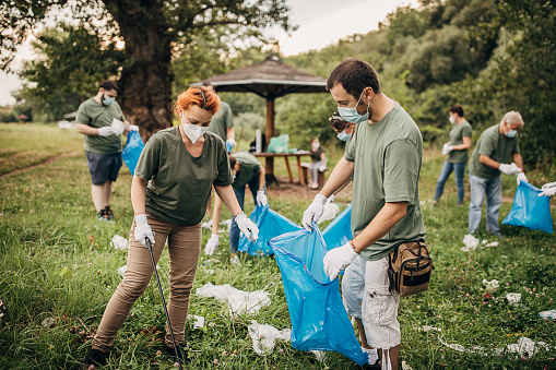 Group of people, environmental volunteers, with protective face masks and gloves collecting garbage from the public park. Be responsible, save our planet and yourself from the coronavirus.