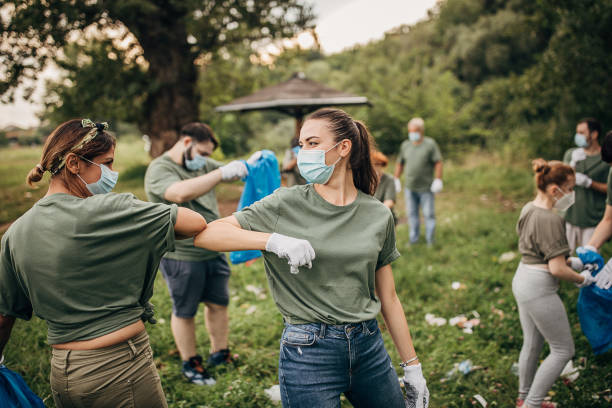 groupe de volontaires avec des masques chirurgicaux nettoyant la nature ensemble - dépollution photos et images de collection