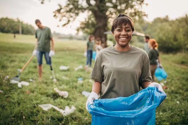 Photo of Portrait of black woman with group of volunteers cleaning nature together