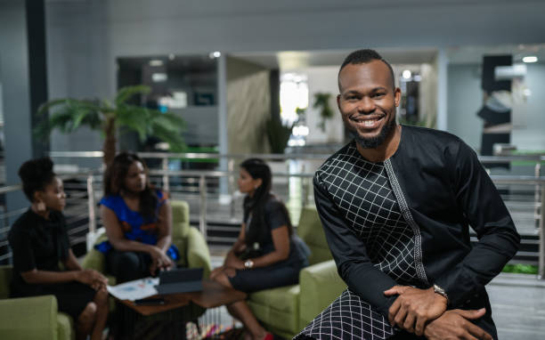 Smiling young African businessman standing in an office with a group of colleagues working in the background