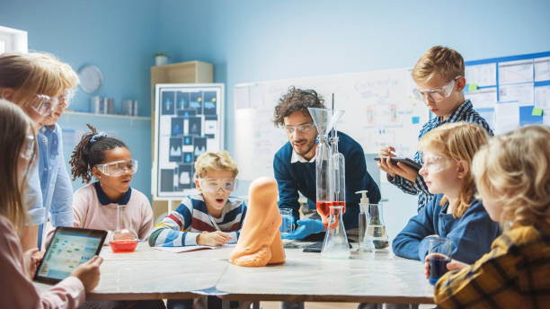istock Elementary School Chemistry Classroom: Enthusiastic Teacher Teaches Diverse Group of Children Shows Science Reaction Experiment by Mixing Chemicals in Beaker so they Shoot Foam (Elephant Toothpaste) 1265582001