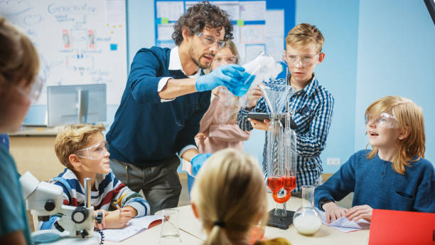 istock Elementary School Science Classroom: Enthusiastic Teacher Explains Chemistry to Diverse Group of Children, Shows them How to Mix Chemicals in Beakers. Children Use Digital Tablet Computers and Talk 1265582065