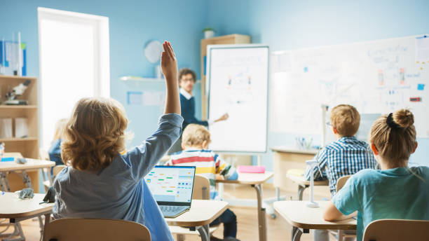 istock Elementary School Physics Teacher Uses Interactive Digital Whiteboard to Show to a Classroom full of Smart Diverse Children how Generator Works. Science Class, Kid Raises Hand with Answer 1265582215