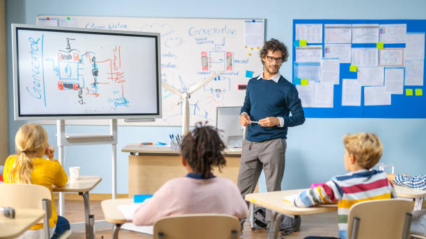 elementary school physics teacher uses interactive digital whiteboard to show to a classroom full of smart diverse children how renewable energy works. science class with kids listening - physics classroom teaching professor imagens e fotografias de stock