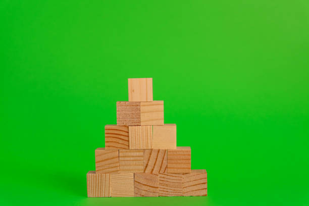 istock Pyremid Construction made of wooden cubes on green background with copy space. Mockup composition for design 1265597099