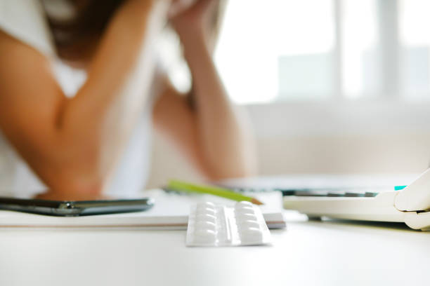 istock White blisters with pills on working table over blur unemployed depressed woman 1265601057