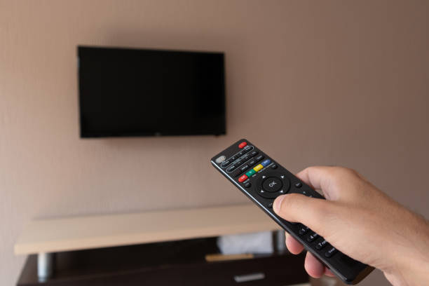 istock Male hand with tv remote control and blurred television 1265602463