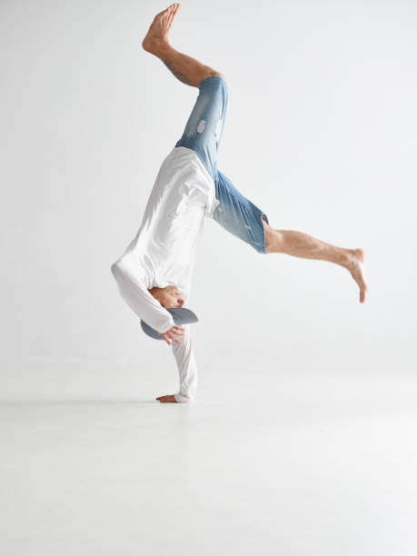 istock Young breakdancer stands on one hand upside down dancing hip-hop isolated on white background. Break dance school poster 1265604506