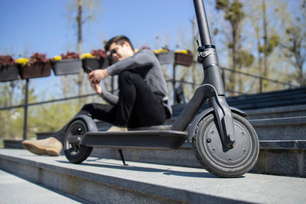 istock Electric scooter commuting vehicle and young man sitting in background using smart phone. 1265607963