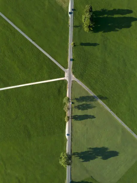 Photo of Aerial top down view of roads crossing in village countryside between green meadows fields. Neuschwanstein district, Bavaria, european Alps, Germany. Europe. Summer time. shadows from trees.