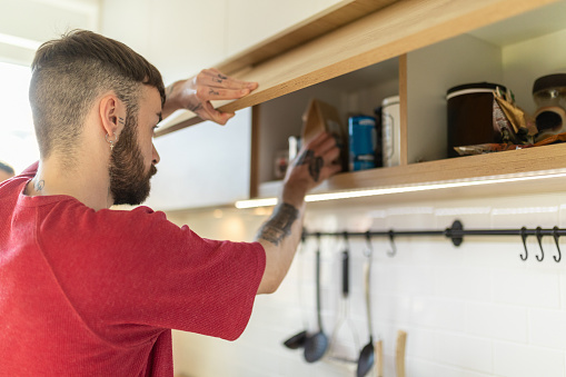 Young man opening upper kitchen cabinet and taking coffee bag