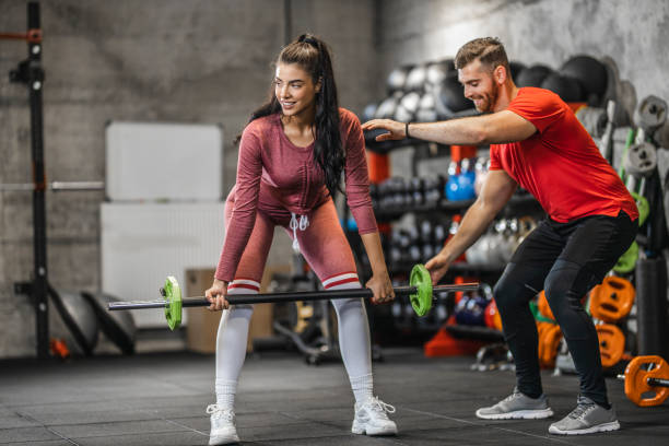 istock Woman lifting barbell while personal trainer assisting her in gym 1265616782