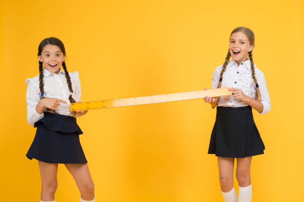 istock distance between us. Ready to study. Kids in uniform measuring. school friendship. happy small girls study mathematics. students use yellow ruler. stem disciplines. back to school. Maths and geometry 1265617770