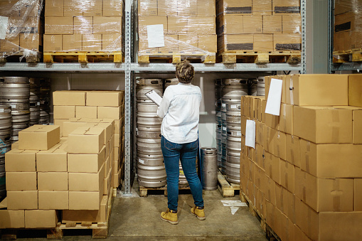 Mid adult woman manager with checklist in brewery distribution warehouse checking supplies