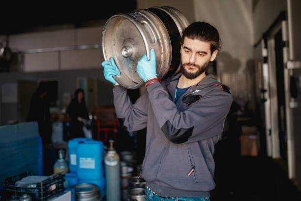 istock Young man in brewery warehouse carrying aluminum barrel on shoulder 1265618265