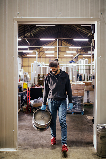 Young man carrying aluminum keg out of the brewery distribution warehouse