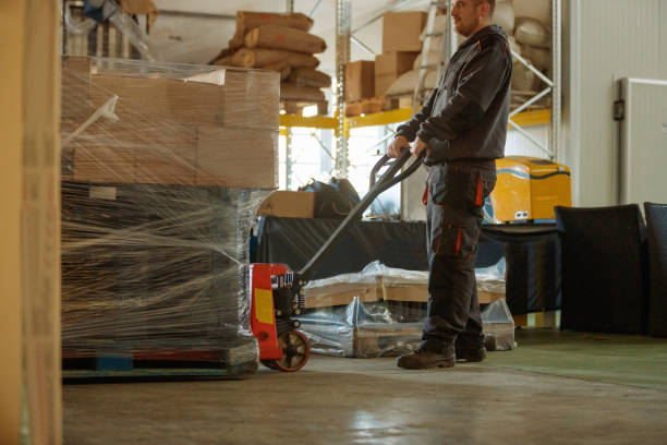 Young man pulling boxes on pallet jack in brewery warehouse Young man pulling wrapped boxes on pallet jack backwards in brewery warehouse pallet jack handle stock pictures, royalty-free photos & images