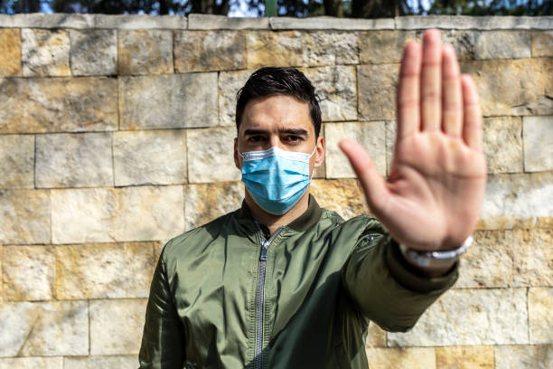 istock Stop the infection! Man with a mask gesturing stop - COVID-19 1265619082