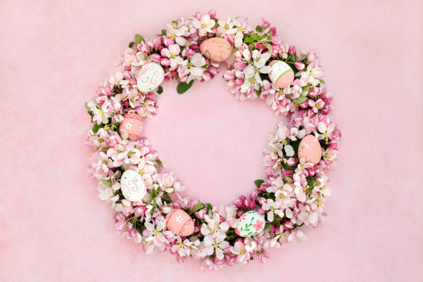 Easter wreath with spring apple blossom flowers & decorated eggs on mottled pink background.