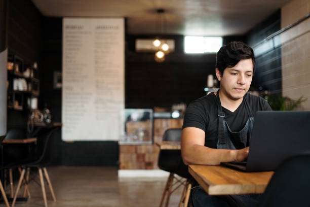 istock Young latin waiter using laptop in coffee shop 1265620682
