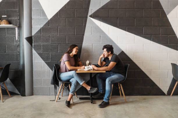 casal adorável sentado à mesa em café e sorrindo um para o outro - table restaurant chair people - fotografias e filmes do acervo