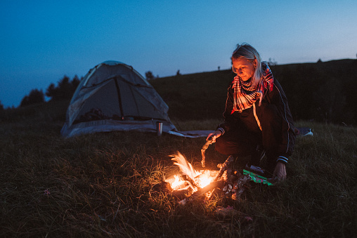 Young woman is  making fire while camping outdoors