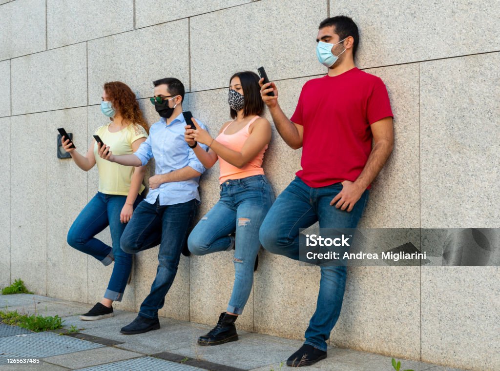 group of millennials girls and boys using their smarthphones during the corona virus outbreak period, use of prevention masks by young people, concept of new sociality and normality 20-29 Years Stock Photo