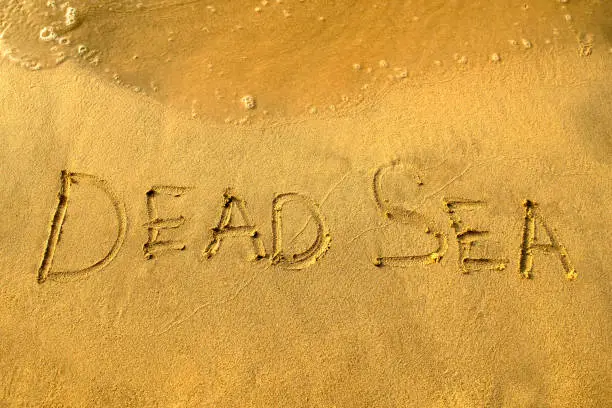 Photo of Dead Sea phrase is written on a sand with water waves.