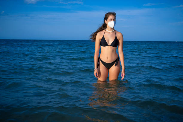 garota turista de biquíni em pandemia com máscara facial n95 em uma bech azul - bech - fotografias e filmes do acervo