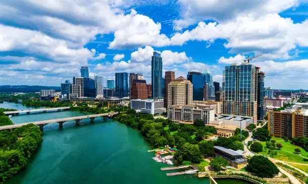 Aerial drone views with green Trees and summer landscape , bright colorful Colorado River and bridges connecting north and south Austin , Texas , USA The downtown Skyscrapers and partly cloudy skies , a beautiful sunny day in Central Texas
