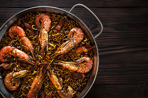 Fidegua pasta paella recipe in a pan with shrimp squid and seafood a Mediterranean food Spain on dark wood