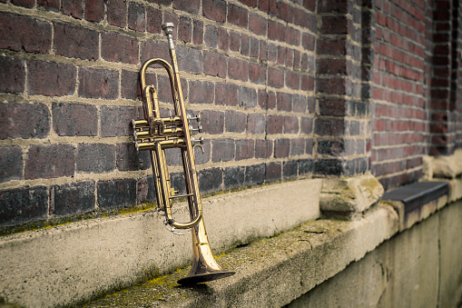 Old rusty Jazz instrument trumpet leaning against brick wall building outside club