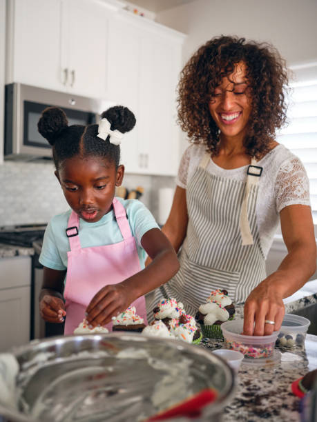Mother and Daughter Baking Cupcakes in a Home Kitchen An African-American mother and daughter bake cupcakes in their home kitchen. decorating a cake photos stock pictures, royalty-free photos & images