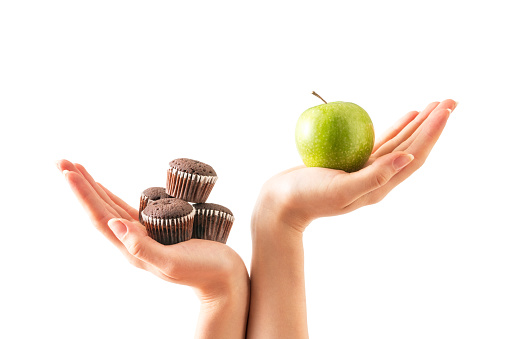 Healthy versus unhealthy. Woman hand holding cake and green apple.