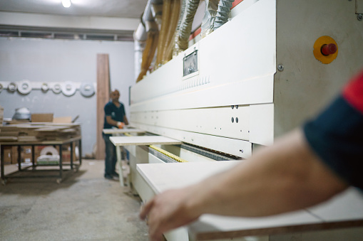 Carpenter in furniture factory working on veneer machine